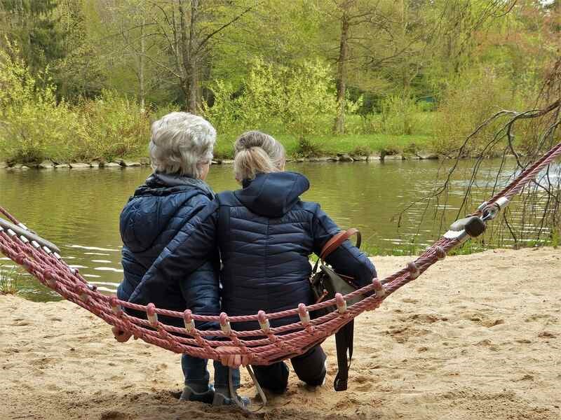 senior woman and her daughter sit on hammock and watch nature