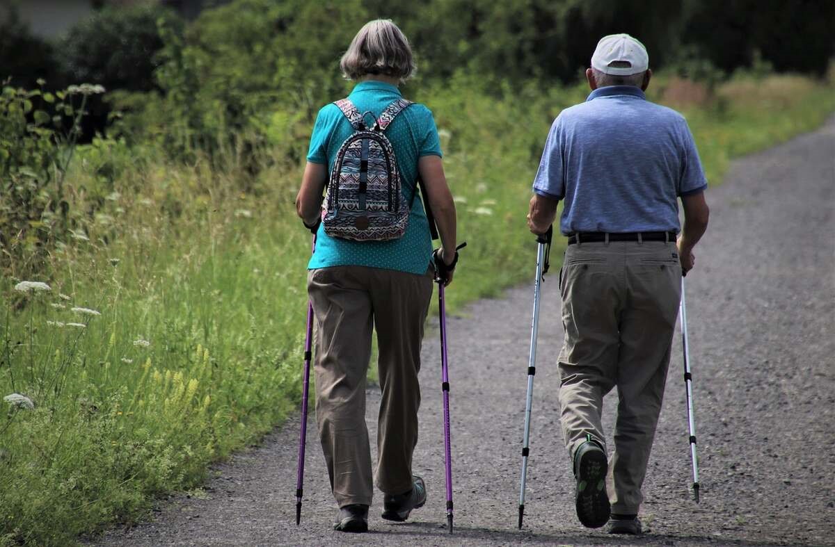 older adults walking on a pathway near a prairie using walking sticks