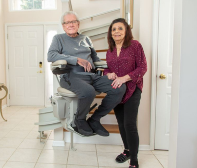 senior couple smiling together with husband sitting on stair lift