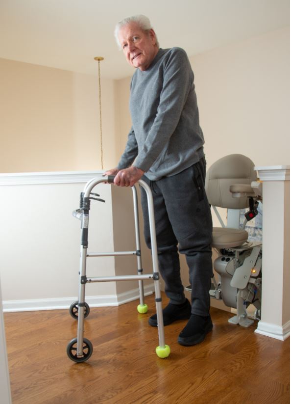 man using walker at top landing of stairs as he exits stair lift from Lifeway Mobility